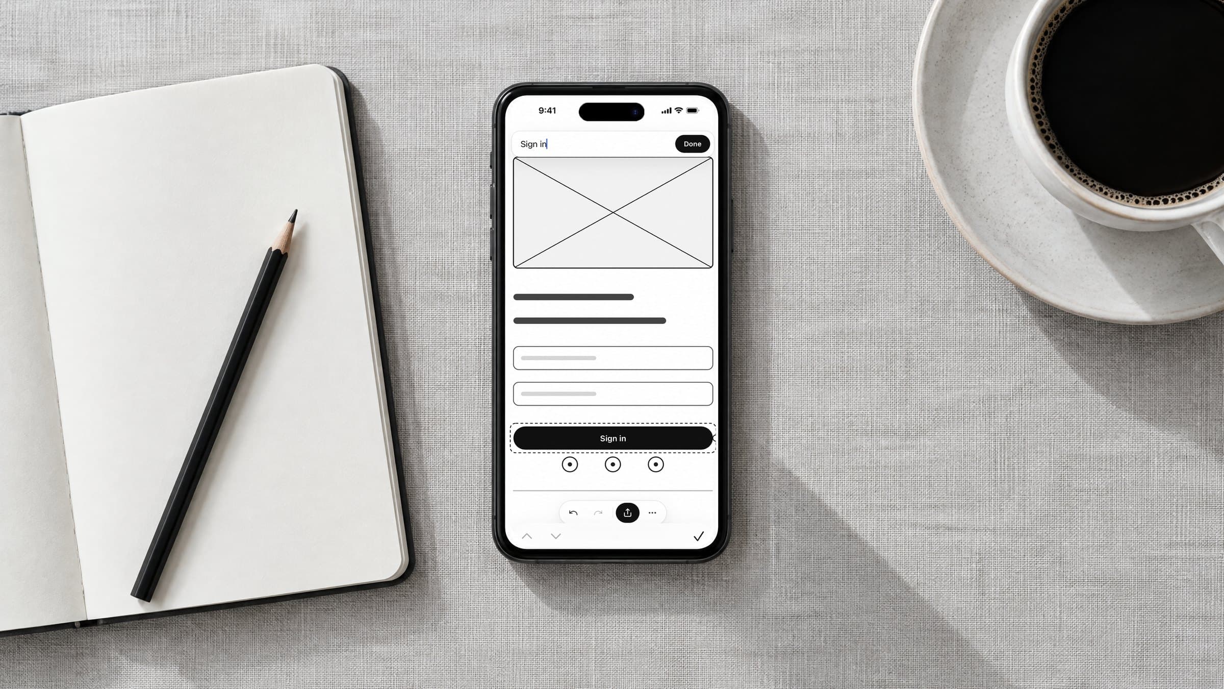 An iPhone showing a DoodleWire sign in wireframe on a desk beside a notebook and coffee